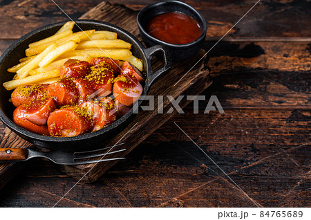 Currywurst Sausages with Curry spice on wursts served French fries in a pan. Dark wooden background. Top view. Copy space Currywurst Sausages with Curry spice on wursts served French fries in a pan. Dark wooden background. Top view. Copy space 84765689