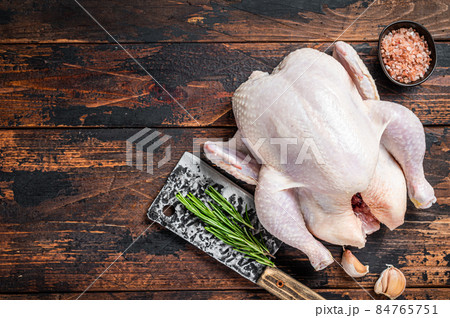Whole chicken, raw poultry on a butchery table with meat cleaver. Dark Wooden background. Top view. Copy space 84765751