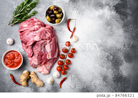 Raw lamb shoulder meat ready for baking, with ingredients and herbs, on gray stone table background, top view flat lay, with copy space for text 84766321
