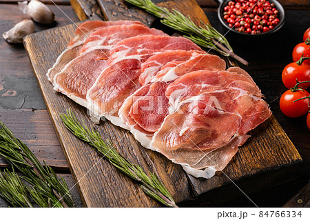 Dry cured Prosciutto crudo parma ham, on old dark wooden table background Dry cured Prosciutto crudo parma ham, on old dark wooden table background 84766334