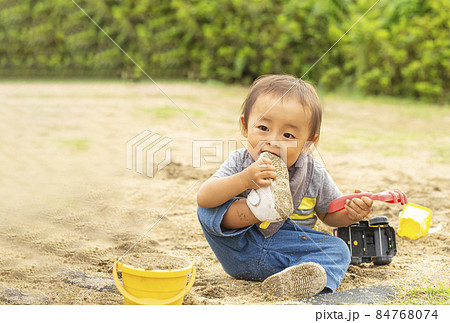 砂場で遊びながら 自分の履いている靴に噛みつく男の子 汚れた靴を口に入れるの写真素材