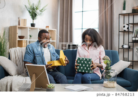 Surprised couple opening gift boxes while sitting on couch 84768213
