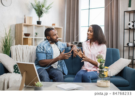 African american couple sitting on couch and chatting African american couple sitting on couch and chatting 84768233