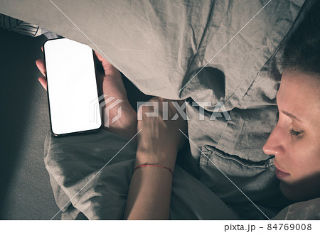 A woman falls asleep in bed with a smartphone in her hand. A woman falls asleep in bed with a smartphone in her hand. 84769008