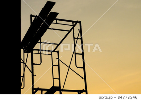 Silhouette of steel scaffolding with wooden plate at the construction site isolated on sunset sky. Day off 84773546