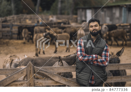 A farmer in the black vest and a plaid shirt standing near the cattle-pen A farmer in the black vest and a plaid shirt standing near the cattle-pen 84777336
