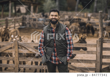 A farmer in the black vest and a plaid shirt standing near the cattle-pen A farmer in the black vest and a plaid shirt standing near the cattle-pen 84777341