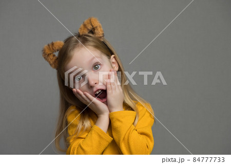 Cute blond girl with tiger ears. A headdress with tiger ears. New Year 2022. Child in a tiger costume smiles sweetly and looks at camera. Cute blond girl with tiger ears. A headdress with tiger ears. New Year 2022. Child in a tiger costume smiles sweetly and looks at camera. 84777733