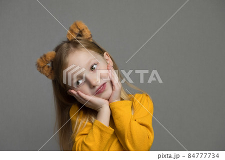 Cute blond girl with tiger ears. A headdress with tiger ears. New Year 2022. Child in a tiger costume smiles sweetly and looks at camera. Cute blond girl with tiger ears. A headdress with tiger ears. New Year 2022. Child in a tiger costume smiles sweetly and looks at camera. 84777734