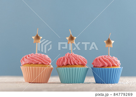 Festive postcard with three pink muffins and candles in the shape of stars on blue background. Copy space. Festive postcard with three pink muffins and candles in the shape of stars on blue background. Copy space. 84779269
