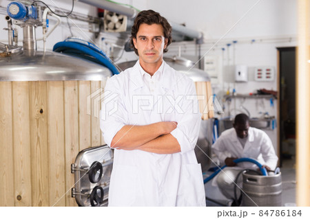 Young man brewer in uniform is standing with glass of beer Young man brewer in uniform is standing with glass of beer 84786184