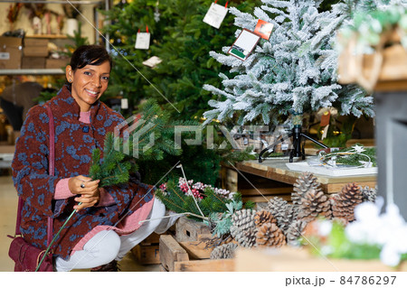 Woman squatting in home goods store near christmas trees Woman squatting in home goods store near christmas trees 84786297