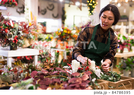 Asian woman seller decorates a Christmas composition with candles Asian woman seller decorates a Christmas composition with candles 84786395
