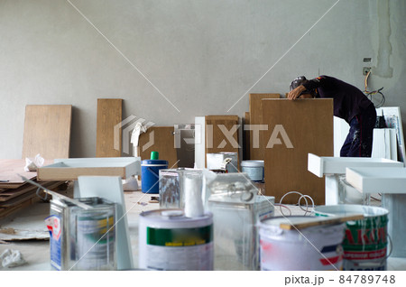 Worker making the wooden board for interior furnitures in the house under construction with blurred foreground of color tanks Worker making the wooden board for interior furnitures in the house under construction with blurred foreground of color tanks 84789748