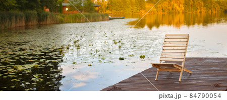 Wooden dock with lounge chair on pier on the calm lake in the middle of the forest 84790054