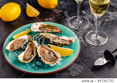 Opened fresh oysters on a blue plate, served with lemon and ice. 84791732