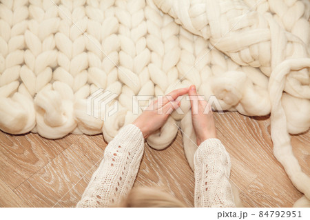 Women's hands knit a plaid of merino wool of large knitting on a wooden floor, top view flat lay. Master class step by step, training 84792951