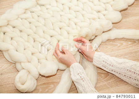 Women's hands knit a plaid of merino wool of large knitting on a wooden floor, top view flat lay. Master class step by step, training 84793011