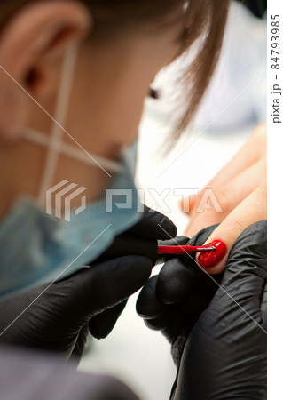 Painting nails of a woman. Hands of Manicurist in black gloves applying red nail polish on female Nails in a beauty salon. 84793985