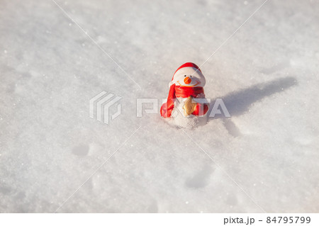 The snowman toy stands on the snow cover in sunny winter evening on sunset. Minimalistic snow background with snowman 84795799