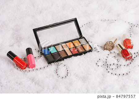 Composition with decorative cosmetics: lipstick, nail polishes, eyeshadow palette and christmas decor in the snow Composition with decorative cosmetics: lipstick, nail polishes, eyeshadow palette and christmas decor in the snow 84797557
