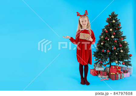 Cute little girl on blue background with Christmas tree and gifts 84797608