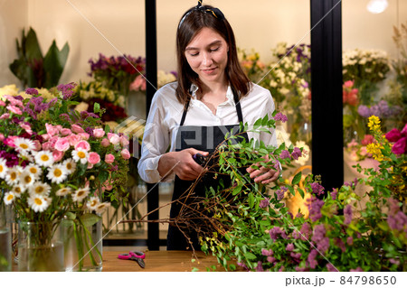 Photo of successful modern florist wearing apron making creating bouquet of flowers Photo of successful modern florist wearing apron making creating bouquet of flowers 84798650