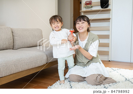 自宅のリビングのラグに座るママとママの横に立って笑う2歳の女の子 84798992