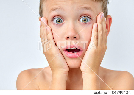 Excited young boy touching cheeks, looking surprised, posing at camera, close-up 84799486