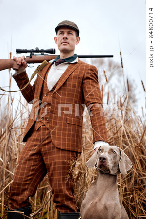 portrait of handsome guy in suit with gray dog on hunting, looking at side. down view portrait of handsome guy in suit with gray dog on hunting, looking at side. down view 84800714