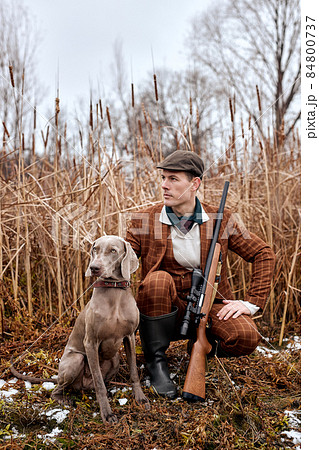 Confident american hunter man with dog holding shotgun rifle walking in countryside 84800737