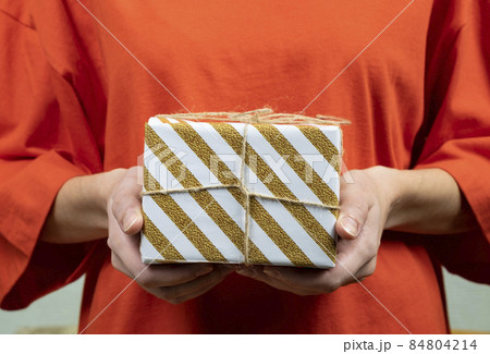 Female hands hold a gift box wrapped in striped paper. Close-up 84804214
