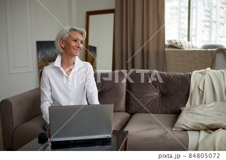 Adult cheerful woman working on laptop at home 84805072