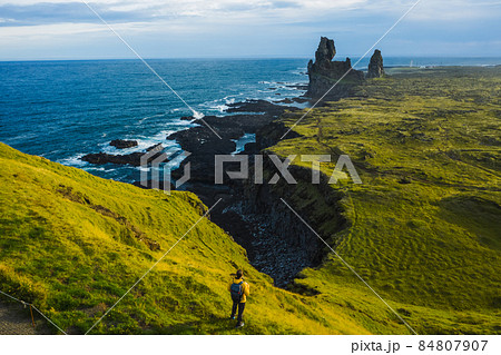 Man hiker in yellow jacket stand on the peak of the rock in outdoor park in Iceland. Londrangar Man hiker in yellow jacket stand on the peak of the rock in outdoor park in Iceland. Londrangar 84807907