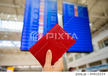 Woman holding a passport against the background of an airport information board. 84810254