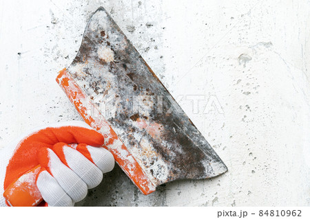 Unrecognizable hand of plasterer holds an old special putty knife and scrapes concrete interior wall, removes old plaster during redecoration of building. Closeup view, selective focus on work tool Unrecognizable hand of plasterer holds an old special putty knife and scrapes concrete interior wall, removes old plaster during redecoration of building. Closeup view, selective focus on work tool 84810962