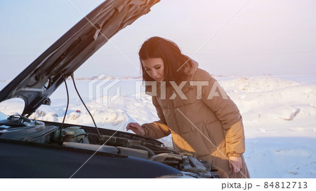 Lady looks at engine of broken automobile on snowy road Lady looks at engine of broken automobile on snowy road 84812713