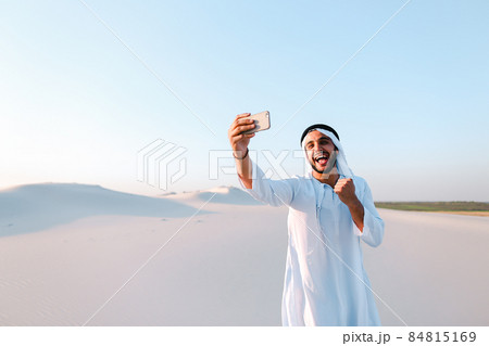 Portrait of Arabian sheikh man with gadget that communicates in skype against blue sky on summer day. 84815169