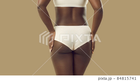 Closeup back view plus size black female model in underwear. Close up backview attractive young African woman wearing white natural cotton underpants standing isolated on solid beige color background 84815741