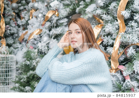 New Year portrait of beautiful caucasian young woman in cozy wool warm light blue sweater. Christmas tree on the background. Christmas shoot New Year portrait of beautiful caucasian young woman in cozy wool warm light blue sweater. Christmas tree on the background. Christmas shoot 84815937