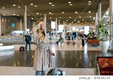 Pretty woman walking in airport waiting room with valise and wea 84816216