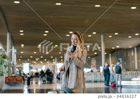 Girl in airport hall standing with valise and using smartphone. 84816227