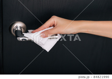 Cleaning black door handles with an antiseptic wet wipe. Sanitize surfaces prevention in hospital and public spaces against corona virus. Woman hand using towel for cleaning home room door link. 84821990