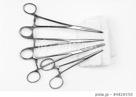 Lot of stainless surgical needle drivers lying on white sterile gauze swab. Medical instruments needle holders on white background. Healthcare and medicine concept. Flat shot, selective focus 84826550