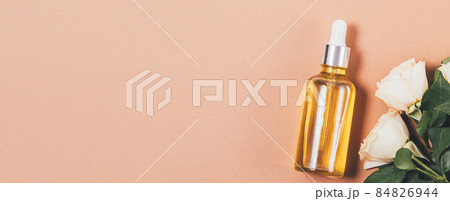 Flat lay cosmetic oil bottle next to fresh roses 84826944