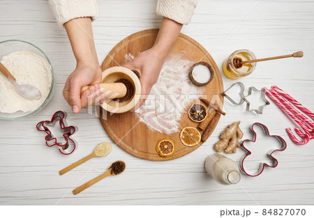 Top view of woman's hands grinding spices and ingredients in a marble mortar, while preparing Christmas cookies in the kitchen table 84827070