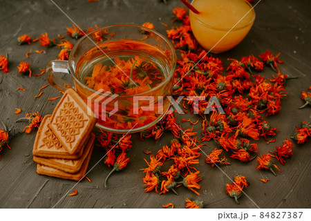 Tea with calendula flowers and biscuits. Transparent glass cup and saucer 84827387