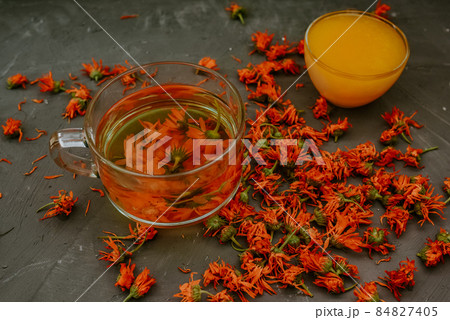 Flower tea in a large transparent mug. A small cup is filled to the top with yellow liquid honey, orange calendula. Flower tea in a large transparent mug. A small cup is filled to the top with yellow liquid honey, orange calendula. 84827405