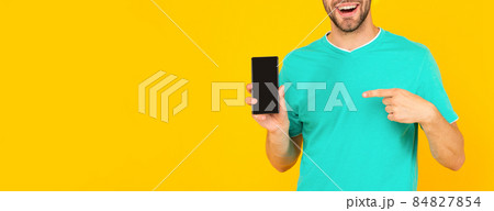 cropped man presenting phone screen. guy point finger on smartphone on yellow background. 84827854