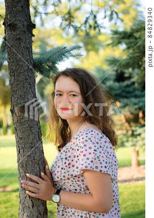 Young brunette girl in dress is posing on tree background in the summer in park 84829340
